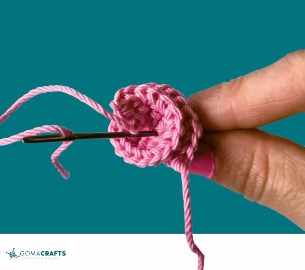 Attaching a pink crocheted flower using a yarn needle for a Magical Unicorn Popsicle crochet project.